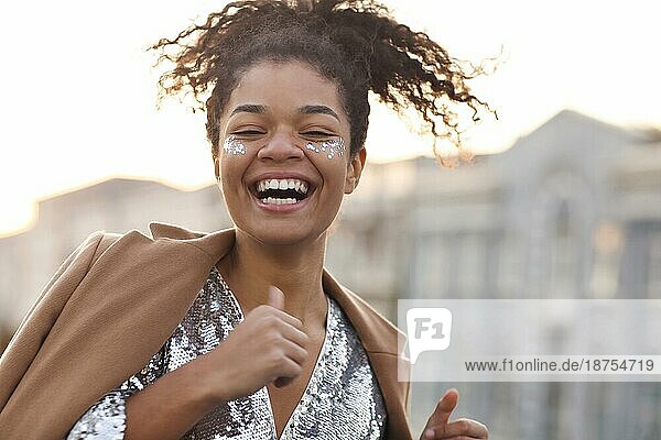 Glück Konzept. Close up Outdoorporträt von glücklichen freudigen afrikanischen amerikanischen Frau mit silbernen glänzenden Glitter auf Gesicht halten die Augen geschlossen und lächelnd glücklich während der Party oder Feier auf dem Dach