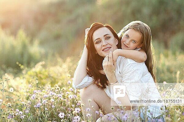 Lächelnde Mutter und Tochter kuscheln sanft auf einer blühenden Wiese  während sie das Wochenende gemeinsam auf dem Land verbringen und in die Kamera schauen