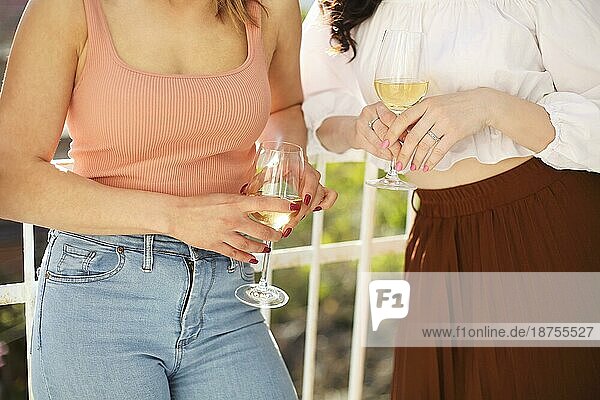 Zwei stilvolle glückliche Frauen versammeln sich im Sommer für eine Party und genießen Zeit zusammen trinken Weißwein