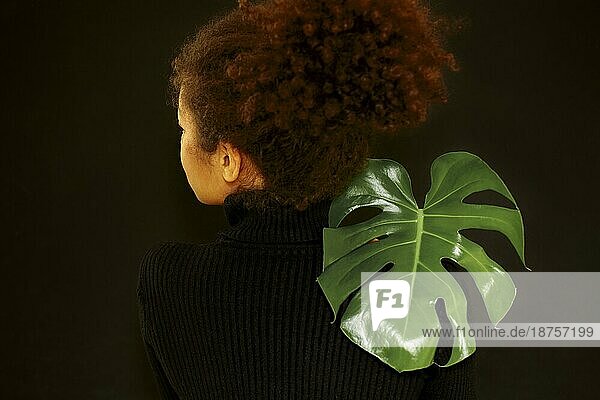 Natürliche Schönheit. Dunkles Studioporträt einer jungen afrikanisch amerikanischen Frau mit grünem Monsterablatt und Blick in die Kamera  nachdenkliche afrikanische Frau  die eine tropische Pflanze hält  isoliert über einer schwarzen Wand