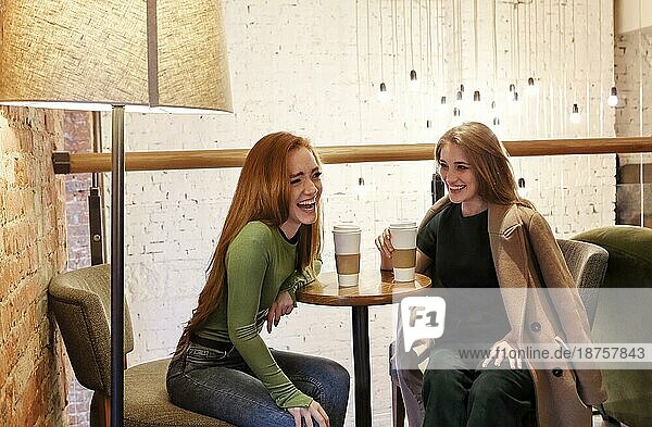 Multiethnische junge Frauen sitzen am Tisch und trinken ein heißes Getränk  während sie sich in einer gemütlichen Cafeteria am Wochenende ausruhen