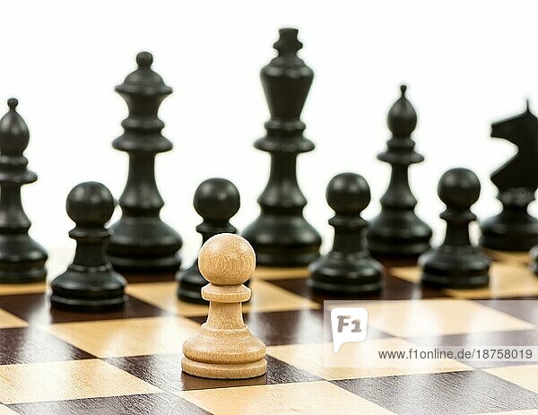 Weißer Baür gegen eine Übermacht von schwarzen Schachfiguren auf einem Schachbrett. Selektiver Fokus