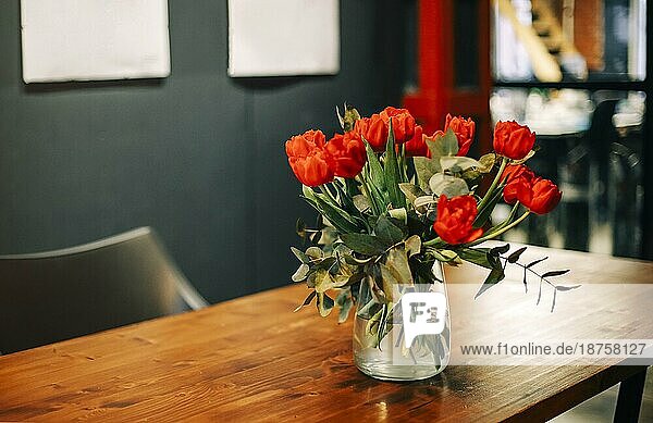 Closeup Foto von Strauß frischer roter Tulpen in Glasvase auf Holztisch im Wohnzimmer Interieur Hintergrund. Frische Schnittblumen für drinnen Dekoration. Florales Arrangement Konzept