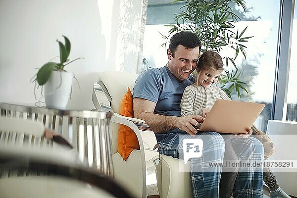Glückliche junge Vater und Vorschüler Tochter sitzen auf Couch beobachten Cartoon auf Laptop zusammen  lächelnd Elternteil Vater genießen Zeit mit kleinen Mädchen Kind lachen auf lustige Video auf Computer entspannen zusammen