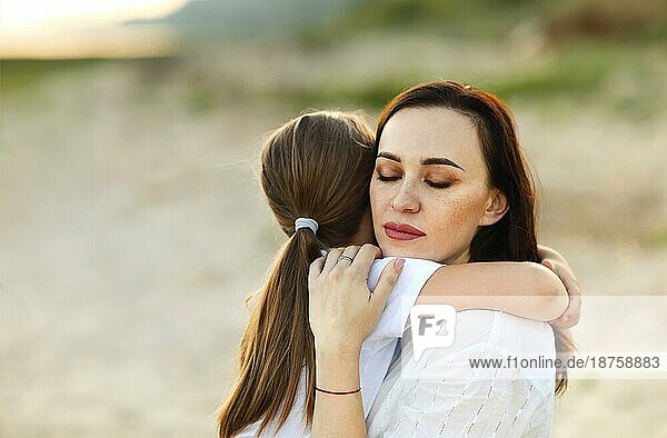 Liebevolle Mutter küsst bezauberndes Mädchen sitzt zusammen am Ufer im Sommer bei Sonnenschein