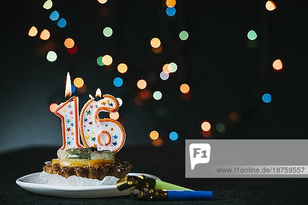 Nummer 16 Geburtstag beleuchtete Kerze Scheibe Torte mit Partei Horn blasen gegen beleuchtete Bokeh Hintergrund