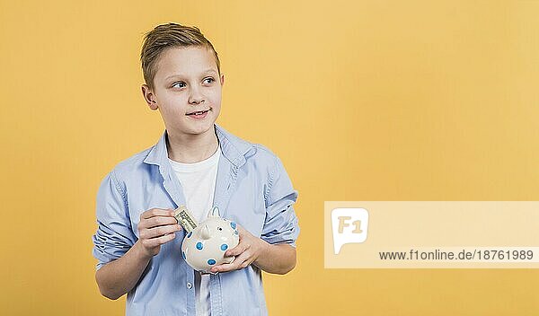 Lächelnder Junge  der Geldscheine in ein weißes Sparschwein aus Keramik einlegt