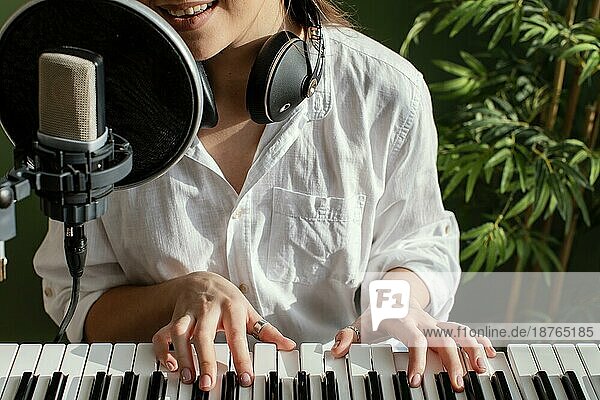 Lächelnde Musikerin  die drinnen auf der Klaviertastatur spielt und ins Mikrofon singt. Foto mit hoher Auflösung
