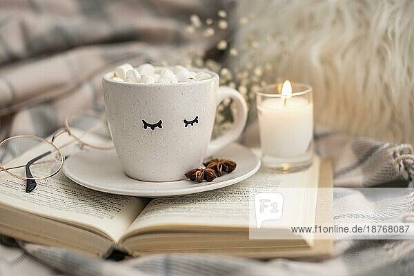 Tasse heißer Kakao mit Marshmallows auf Buch mit Kerze