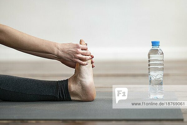 Seitenansicht Frau dehnt Yogamatte mit Wasserflasche. Foto mit hoher Auflösung