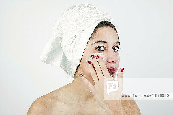 Junge Frau cremt ihr Gesicht mit einem weißen Handtuch ein