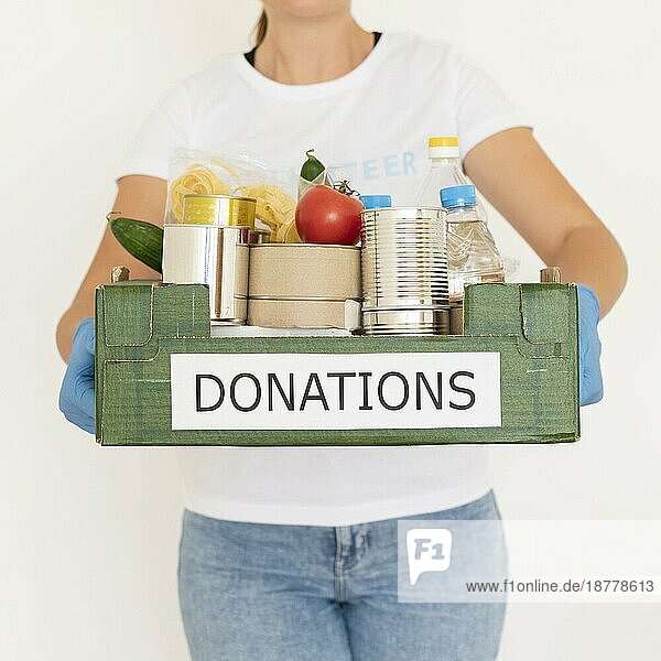 Weibliche Freiwillige mit Handschuhen hält eine Lebensmittelspendenbox