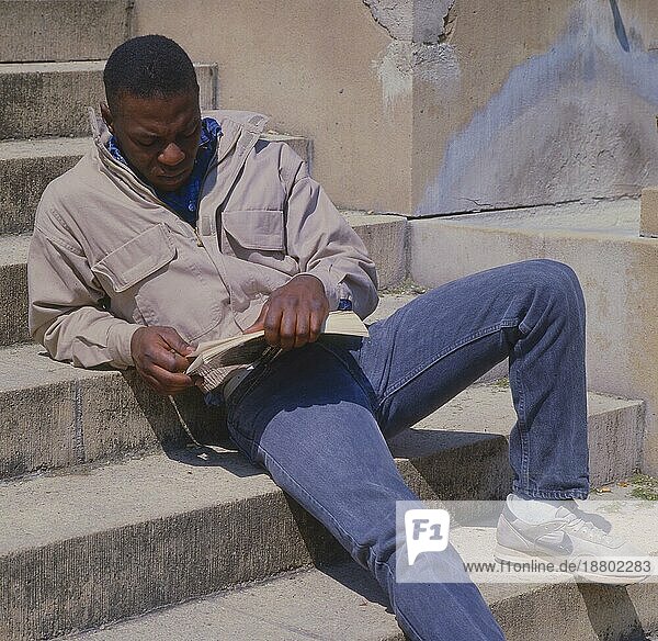 Junger Afrikaner liest in einem Buch  auf einer Treppe