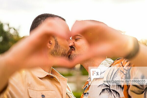 Porträt von Homosexuell Freund und Freundin machen das Herz oder Liebe Geste küssen bei Sonnenuntergang in einem Park in der Stadt. Vielfalt und lgbt Konzept