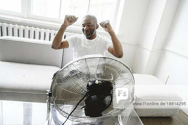 Glücklicher Mann tanzt zu Hause vor elektrischem Ventilator