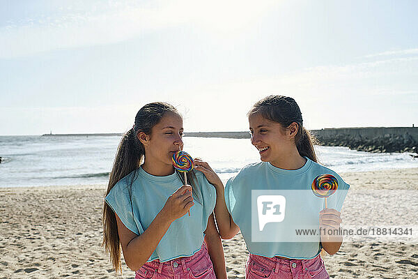 Smiling twin sisters enjoying lollipop candy at beach