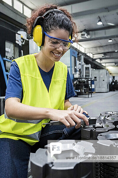 Lächelnder Ingenieur in reflektierender Kleidung  der in einer modernen Fabrik arbeitet