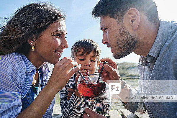 Happy father and mother with son drinking juice on sunny day