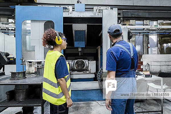 Maintenance engineer examining coworker working on machinery in modern factory