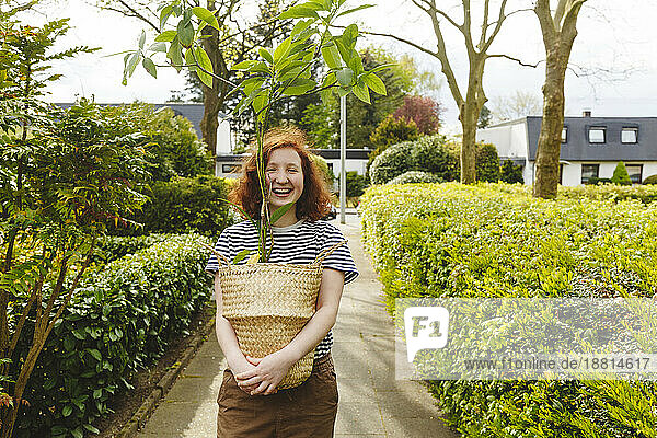 Glückliches Mädchen steht mit Avocadopflanze auf Fußweg