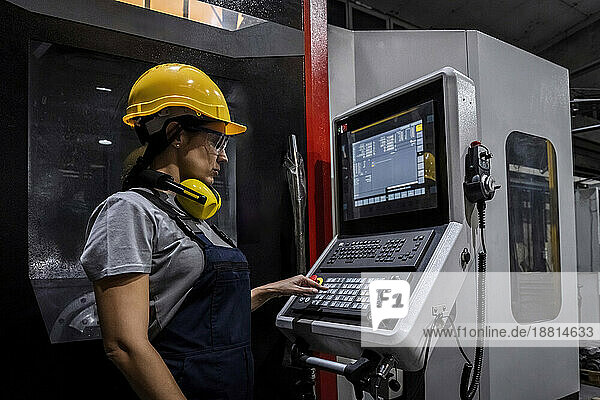 Engineer wearing hardhat operating CNC machine keypad in modern factory