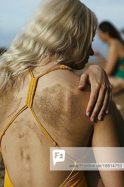 Blond woman with sand on back at beach