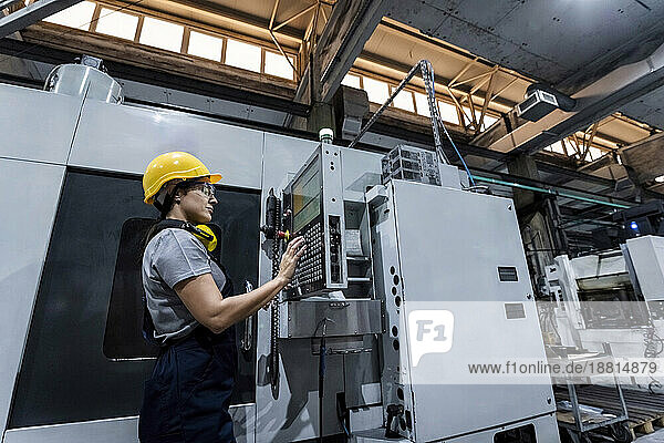 Wartungstechniker mit Schutzhelm und CNC-Maschinentastatur in einer modernen Fabrik