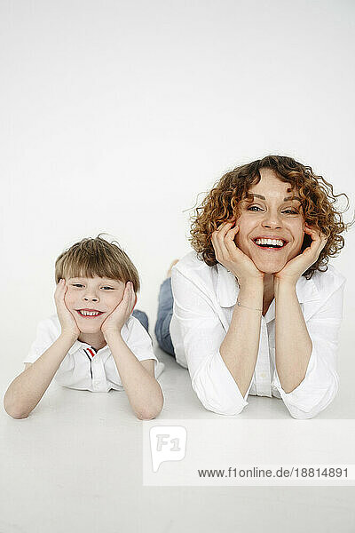 Happy woman lying down with son in front of white backdrop