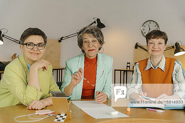 Drei Geschäftsfrauen sitzen am Tisch und schauen in die Kamera