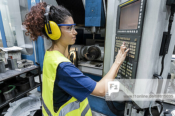 Engineer in protective workwear operating CNC machine in modern factory