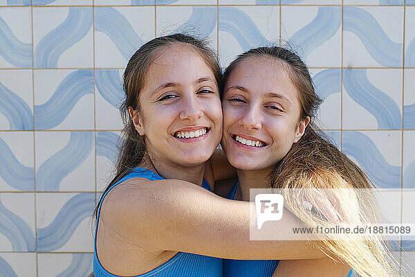 Liebevolle Zwillingsschwestern umarmen sich vor der Wand