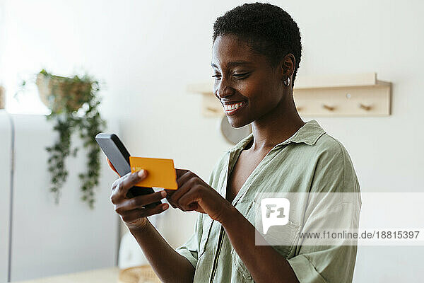 Glückliche Frau  die zu Hause per Kreditkarte auf dem Mobiltelefon bezahlt