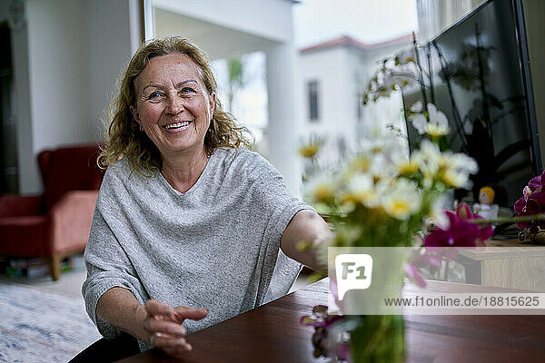 Happy senior woman touching flowers at home