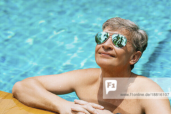 Lächelnder Mann mit Sonnenbrille entspannt sich an einem sonnigen Tag im Schwimmbad