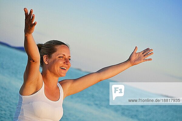 Junge Frau mit erhobenen Händen  die Freude am Strand ausdrücken