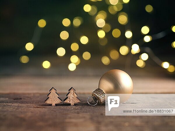Goldene Christbaumkugel mit kleinen hölzernen Baumformen mit verschwommener Weihnachtsbeleuchtung  traditionelle Weihnachtskarte