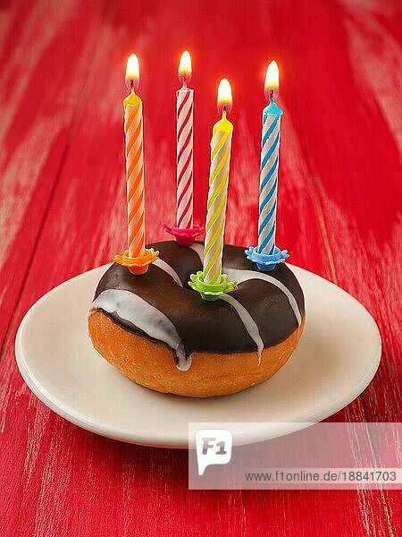 Bunte Geburtstagskerzen mit einem Donut auf einem roten Holztisch