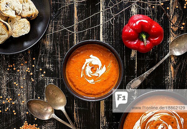 Leckere Kürbissuppe mit viel Sahne auf einem dunklen  rustikalen Holztisch mit roter Paprika  Brottoasts  Linsen und Herbstzweigen. Ansicht von oben