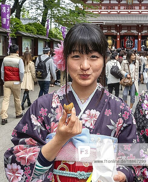 Tokio Japan. Ein Mädchen probiert Süßigkeiten in den Straßen von Asakusa