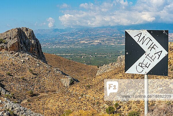 Blick hinunter auf die Messara Ebene auf Kreta. Die Ebene erstreckt sich über 50 km in West Ost Richtung und 7 km in Nord Süd Richtung und ist damit die größte Ebene auf Kreta. Das Straßenschild wird von der Antifa Kreta besprüht