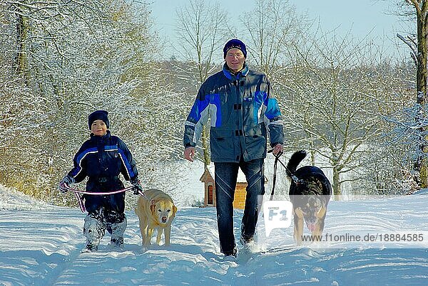Vater mit Mischlingshund  Sohn mit Labrador Retriever  Skianzug  Mütze  spazieren gehen  Labrador-Retriever