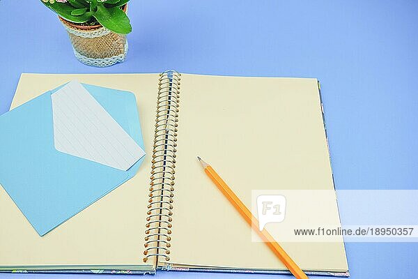 Bleistift auf einem leeren Notizbuch mit einem blauen Umschlag mit einem Brief darin