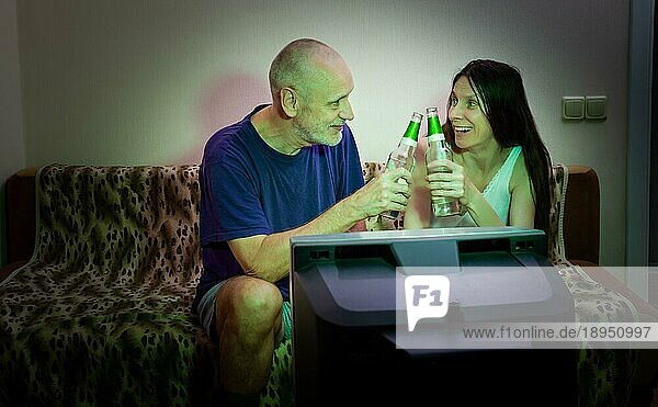 Ein erwachsener Mann und eine Frau sehen sich in ihrer kleinen Wohnung Sport im Fernsehen an. Ihre Lieblingsmannschaft hat das Spiel gewonnen. Sie trinken auf seinen Sieg und lächeln voller Freude und Glück