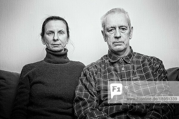 Dramatisches Porträt einer traurigen und deprimierten erwachsenen Frau und eines Mannes  die auf einem Sofa sitzen und mit glanzlosen Augen ins Leere schauen. Negativer Raum für Text