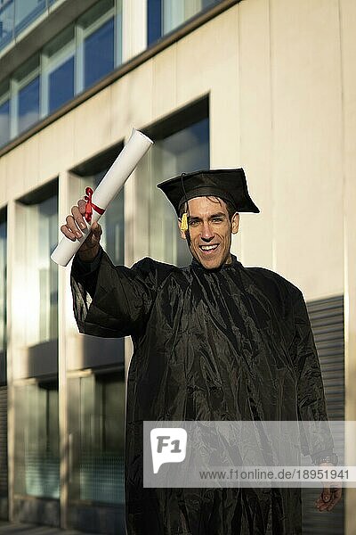 Ein Mann  der vor kurzem seinen Abschluss gemacht hat  trägt Hut und Talar und zeigt sein Diplom  während er feiert