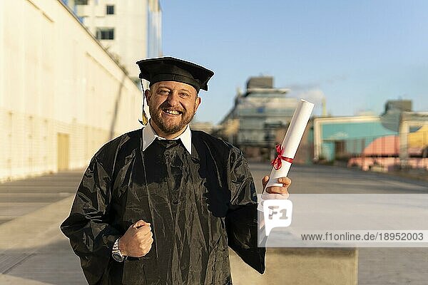 Ein Mann  der vor kurzem seinen Abschluss gemacht hat  trägt Hut und Talar und zeigt sein Diplom  während er feiert