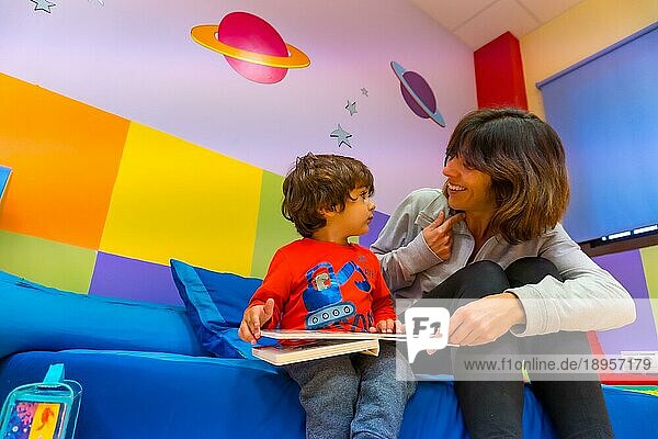 Erzieherin spielt mit einem Kind  das ein Buch liest und Spaß hat  Innenansicht eines Kindergartens