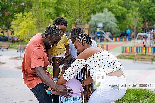 Afrikanische schwarze ethnische Familie mit Kindern auf dem Spielplatz  die sich mit dem Fahrrad umarmen
