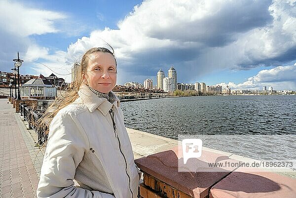 Eine lächelnde Frau steht in der Nähe des Flusses  ihr Haar wird vom Wind bewegt unter einem dramatischen stürmischen Frühlingshimmel