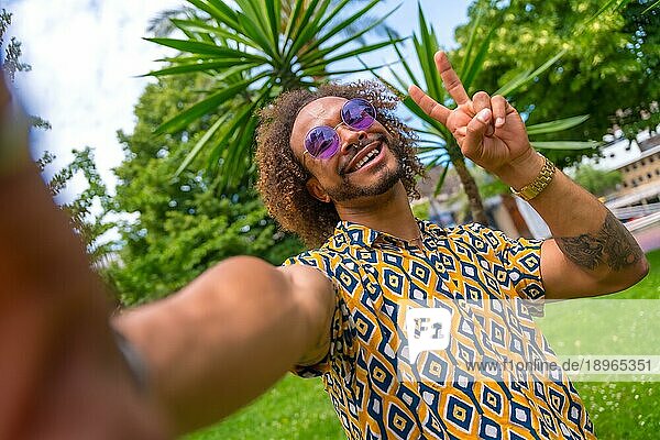 Afro haired Mann im Sommerurlaub neben einigen Palmen am Strand ein Selfie und tun den Sieg selfie. Reisen und Tourismus Konzept